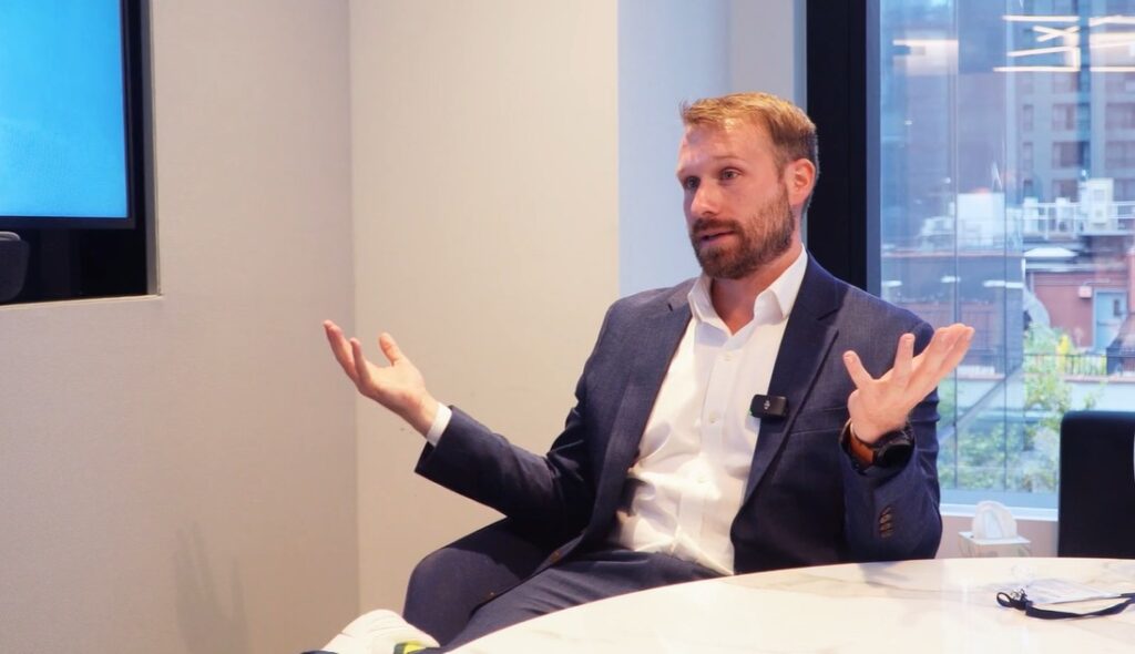 James Seyffart sentado en una sala de reuniones moderna con ventanal al fondo.