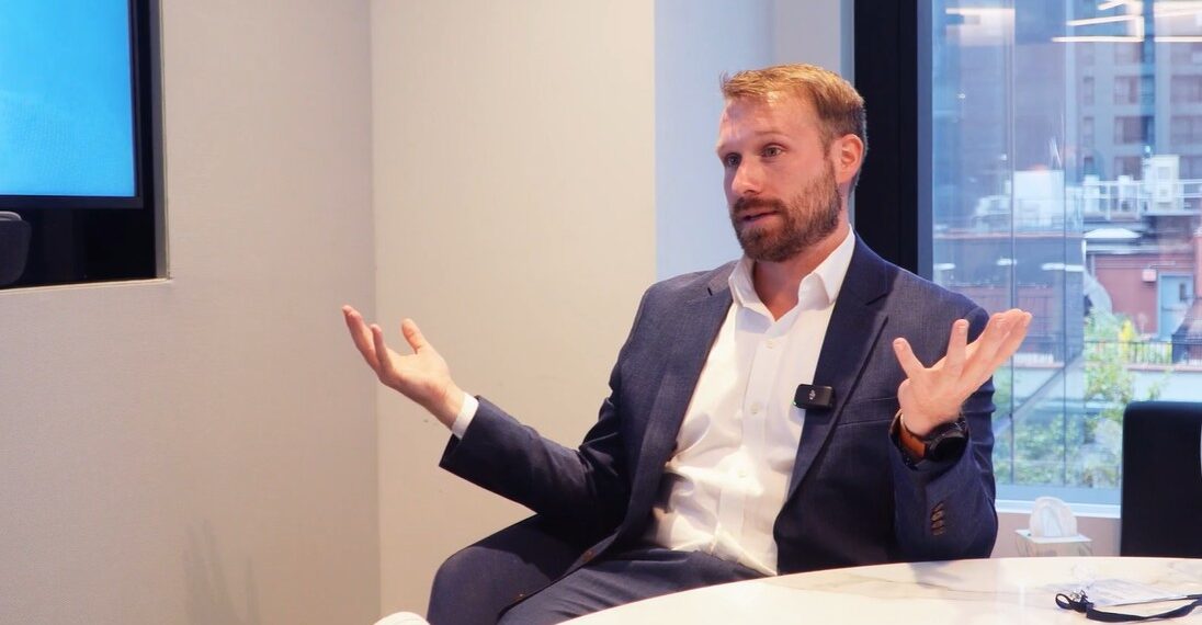 James Seyffart sentado en una sala de reuniones moderna con ventanal al fondo.