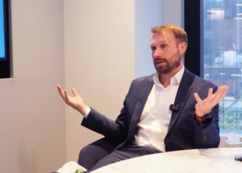 James Seyffart sentado en una sala de reuniones moderna con ventanal al fondo.