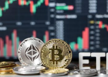 Dos monedas, una de bitcoin (dorada) y otra de ethereum (plateada), sobre otras monedas y letras que forman las siglas "ETF", con gráficos bursátiles de fondo.