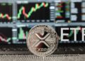 Moneda física de XRP plateada, acompañada por las letras ETF y de fondo pantallas de trading de Wall Street con gráficos.