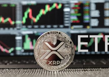 Moneda física de XRP plateada, acompañada por las letras ETF y de fondo pantallas de trading de Wall Street con gráficos.