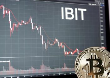Una moneda física de bitcoin dorada y brillante apoyada sobre una superficie oscura; al fondo, una pantalla de trading con un gráfico y destaca en grande y en blanco el ticker «IBIT».