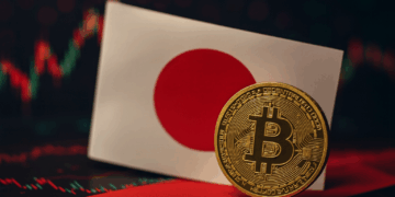 Moneda de Bitcoin en primer plano junto a la bandera de Japón, con gráficos financieros difuminados al fondo