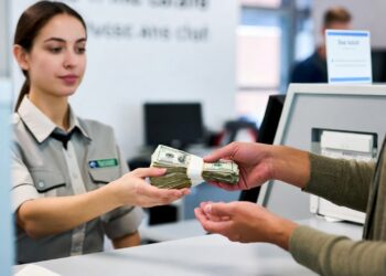 Una persona entrega un fajo de billetes de dólares a una cajera en un mostrador de atención al cliente de un banco.