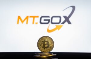 Moneda física de bitcoin dorada sobre un escritorio con el logo de Mt.Gox de fondo.