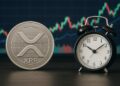 Moneda física de XRP junto a un reloj analógico y de fondo gráficas de mercado.