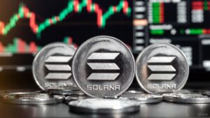 Varias monedas físicas de solana de acabado metálico con un fondo de gráficos de velas bursátiles.