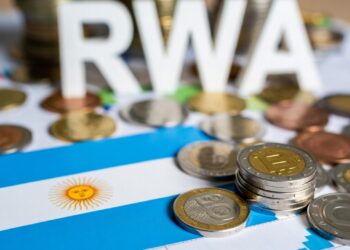 Monedas físicas representativas de bitcoin y otras monedas junto a una bandera de Argentina.