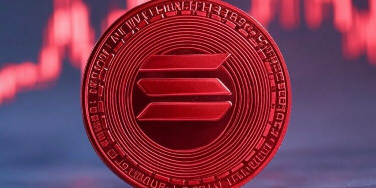 Una moneda física de color rojo de solana delante de un gráfico de precios.