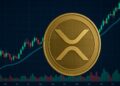 Una moneda física de XRP delante de gráficos de precios.
