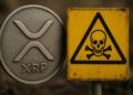Moneda física de XRP al lado de un letrero de peligro de muerte de color amarillo.