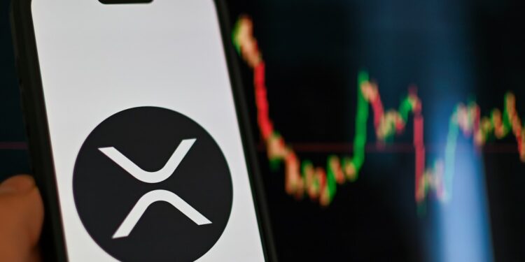 Logo de XRP en la pantalla de un teléfono con un fondo de gráfico de precios..