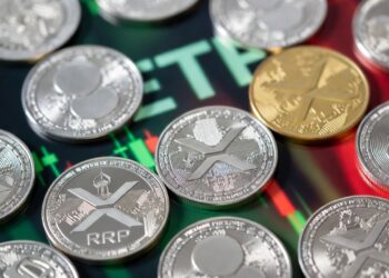 Varias monedas físicas de XRP dispersas y un gráfico bursátil en tonos verdes y rojos.