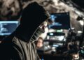 Un hombre con capucha y la cara cubierta frente a una computadora