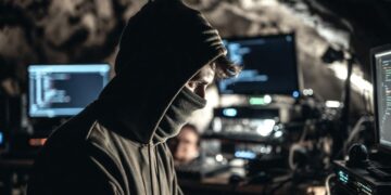 Un hombre con capucha y la cara cubierta frente a una computadora