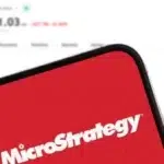 Un móvil con el logo de Microstrategy y en el fondo el precio de bitcoin.