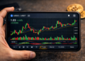 Gráfico de velas de USDC/USDT (tether y circle) en un smartphone sostenido por una mano, con indicadores de trading visibles