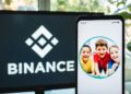 Logo de Binance en un monitor junto a un smartphone que tiene como fondo de pantalla a unos niños.