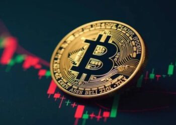 Moneda física de bitcoin dorada sobre gráficos de mercado.