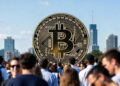 Una multitud rodea a una moneda gigante de bitcoin, con una ciudad al fondo