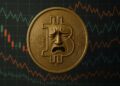 Moneda física de bitcoin dorada con una cara de dolor y de fondo gráficas de mercado.