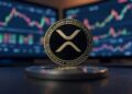 Una moneda física de XRP delante de dos pantallas que muestran gráficos de precio.