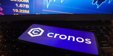 Teléfono móvil con el logo de cronos delante de un gráfico de precio.