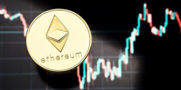 Moneda física de Ethereum dorada sobre gráficos de mercado.