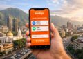 Mano sosteniendo un smartphone con la app Kontigo con la ciudad de Caracas y el cerro Ávila de fondo.