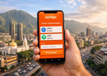 Mano sosteniendo un smartphone con la app Kontigo con la ciudad de Caracas y el cerro Ávila de fondo.