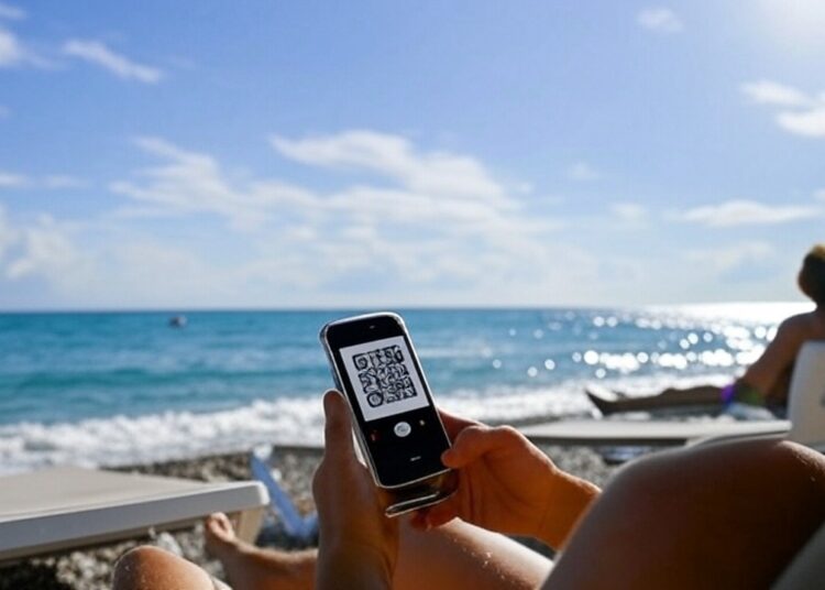 Una persona frente al mar a punto de hacer un pago por QR a través de su celular.