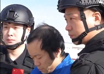 Chen Zhi, acusado de megaestafas con criptomonedas, camina entre dos policías de China.