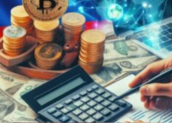 Una persona se ve haciendo cálculos en una mesa junto con monedas digitales doradas dispuestas en un escritorio. Al fondo se observa una bandera de Colombia.