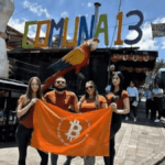 Personas con una bandera naranja de Bitcoin debajo de un que dice Comuna 13 en Medellín Colombia.