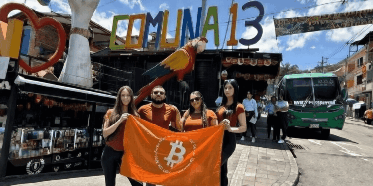 Personas con una bandera naranja de Bitcoin debajo de un que dice Comuna 13 en Medellín Colombia.