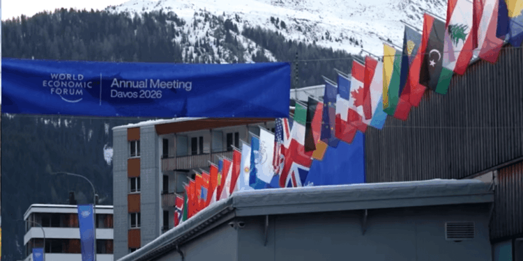 Banderas de varios países del mundo junto a un letrero que dice Annual Meeting Davos 2026 y de fondo los Alpes Suizos.