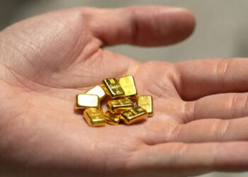 Mano abierta con la palma hacia arriba sosteniendo varios lingotes pequeños de oro puro.