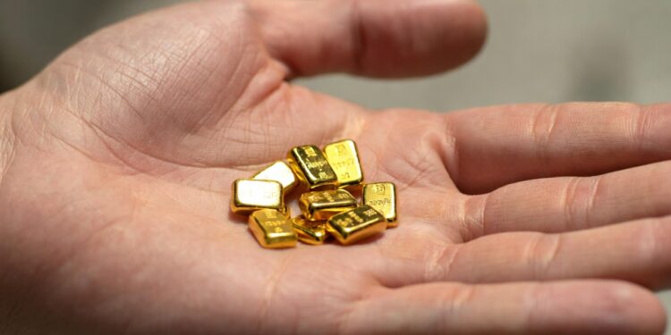 Mano abierta con la palma hacia arriba sosteniendo varios lingotes pequeños de oro puro.