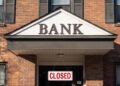 Fachada de un banco por fuera, con un letrero en rojo que dice "cerrado" en inglés
