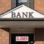 Fachada de un banco por fuera, con un letrero en rojo que dice "cerrado" en inglés