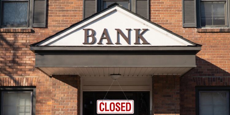 Fachada de un banco por fuera, con un letrero en rojo que dice "cerrado" en inglรฉs