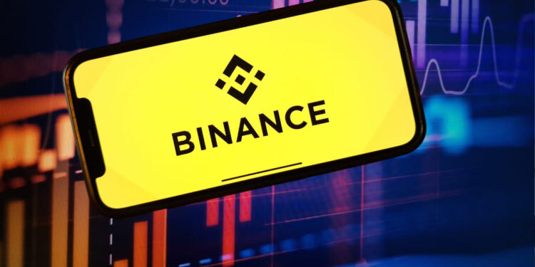 Logo de Binance sobre una pantalla de un móvil con velas rojas y verdes de fondo que reflejan la volatilidad del mercado.