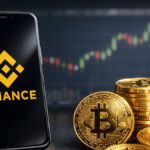 Smartphone con el logo de Binance en pantalla junto a monedas fรญsicas de bitcoin, con grรกficos del mercado de fondo.