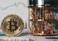 Moneda fรญsica de bitcoin dorada al lado de una computadora cuรกntica y grรกficas de mercado en el fondo.