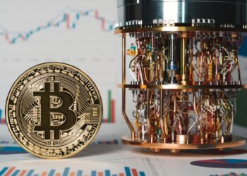 Moneda física de bitcoin dorada al lado de una computadora cuántica y gráficas de mercado en el fondo.