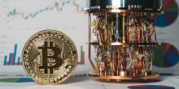 Moneda física de bitcoin dorada al lado de una computadora cuántica y gráficas de mercado en el fondo.
