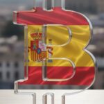 Logo de bitcoin en cristal que muestra la bandera de España y de fondo una ciudad.