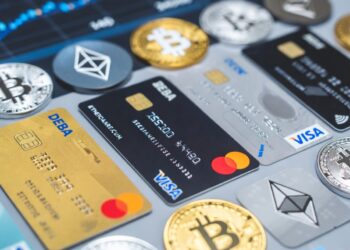 Tarjetas de crédito y débito sobre una mesa con distintas criptomonedas alrededor.