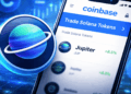 Una moneda física del token Jupiter junto a un celular que muestra la app de Coinbase.